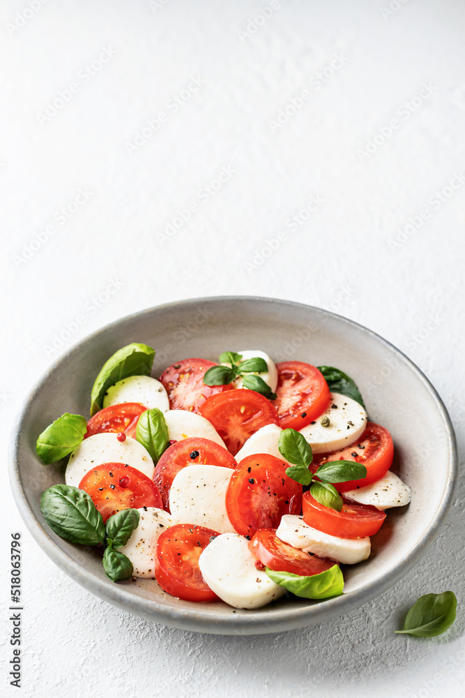 Traditional caprese salad with tomatoes mozzarella basil and olive oil with a basil leaf near on white background. Text space