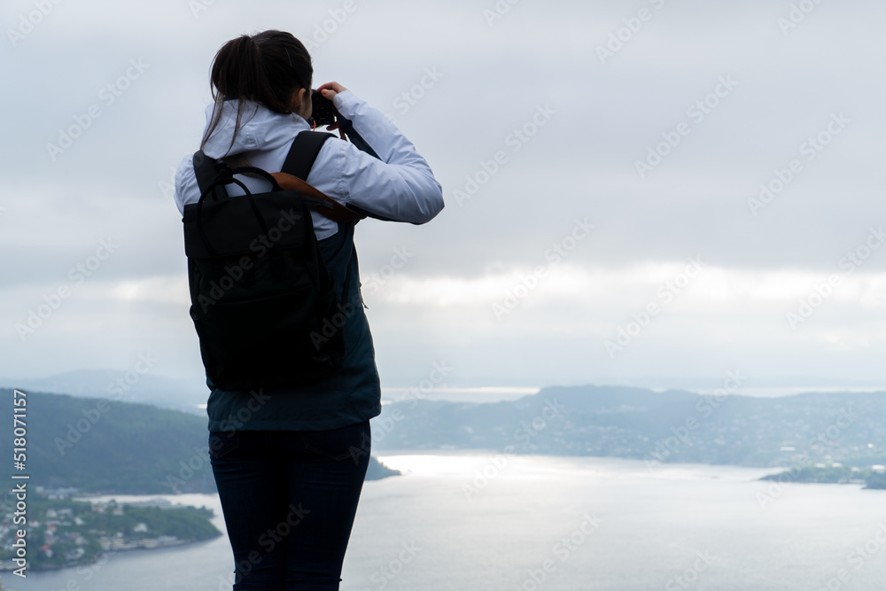 Unrecognizable young woman with his backpack and his camera and photography the city of Bergen and the fjord in Norway