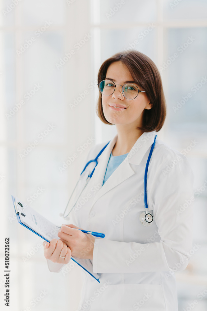 Qualified cardiac expert with stethoscope prepares for health seminar, gives consultancy about first aid, writes down information in clipboard, wears white gown, ready to give medic care help