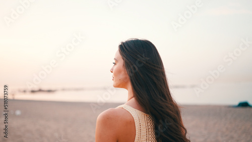 Beautiful brown-haired woman with long hair walks along the beach and looks around. Gorgeous girl with long eyelashes