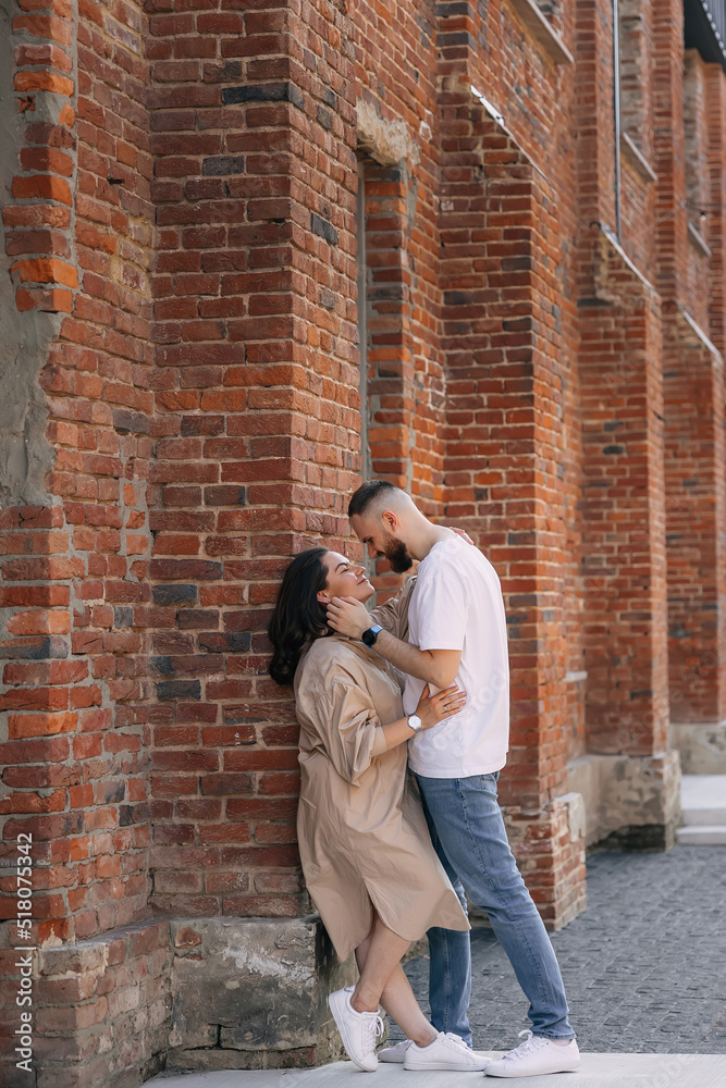 Stylish beautiful fashionable couple in fashionable casual clothes poses together on the street near brick wall