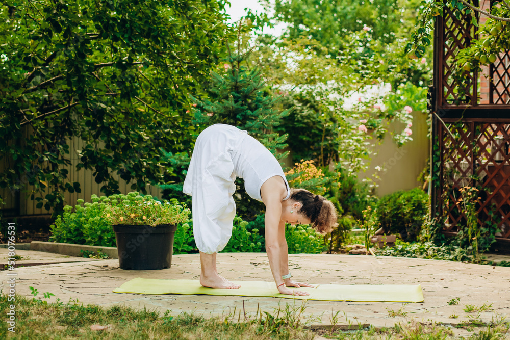 Woman practices yoga in summer garden: Uttanasana, or tilting the head to the feet