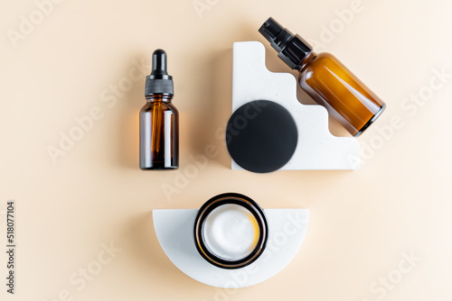 Trendy presentation of cosmetic set for skin care. Top view of dark glass packaging - dropper bottle, cream jar and bottle dispencer fith essence on concrete poduims.
