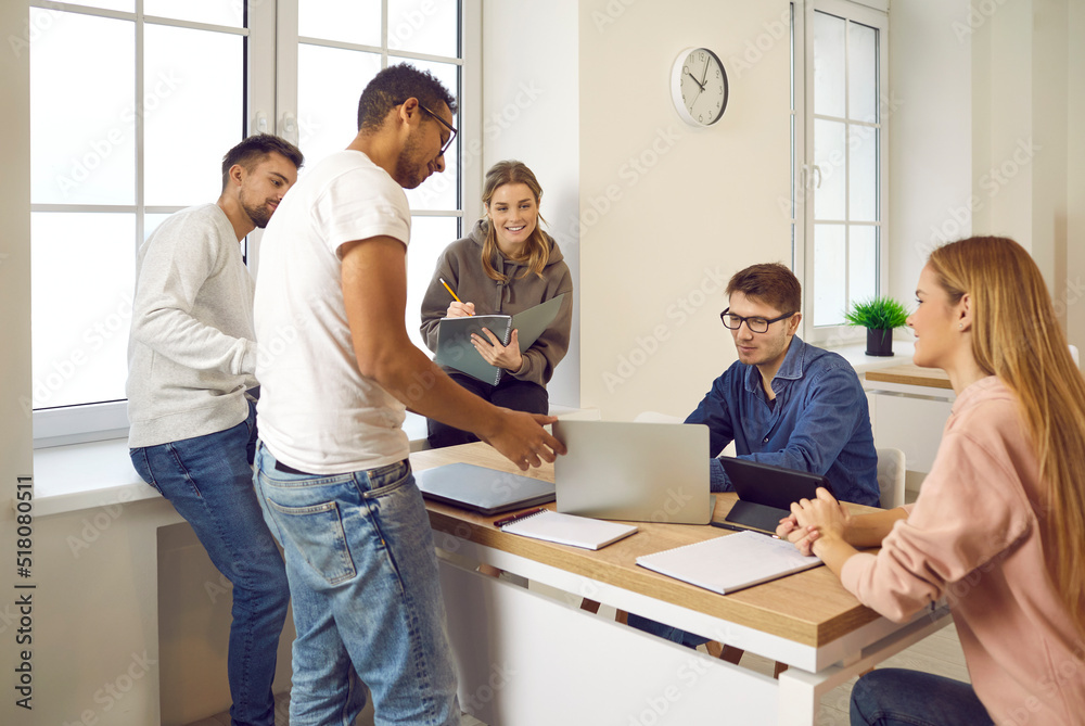 Fototapeta premium Multiracial students study and prepare school project together during study meeting. Girls and boys sitting in front of modern devices communicate and write notes in notebooks. Education concept.