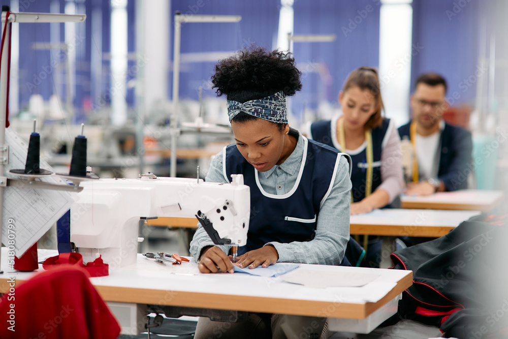 Young black woman works as seamstress at production line in textile factory. Young black woman works as seamstress at production line in textile factory.