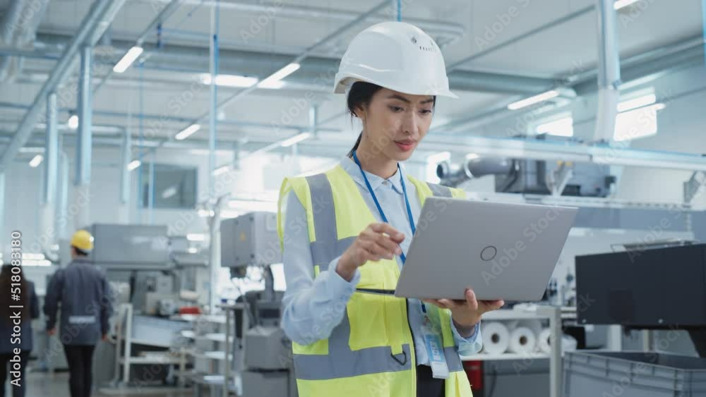 Portrait of a Happy Asian Female Engineer in Hard Hat Standing and Using Laptop Computer at Electronic Manufacturing Factory. Technician Thinking About Daily Tasks and Working on Development Pipeline. Portrait of a Happy Asian Female Engineer in Hard Hat Standing and Using Laptop Computer at Electronic Manufacturing Factory. Technician Thinking About Daily Tasks and Working on Development Pipeline.
