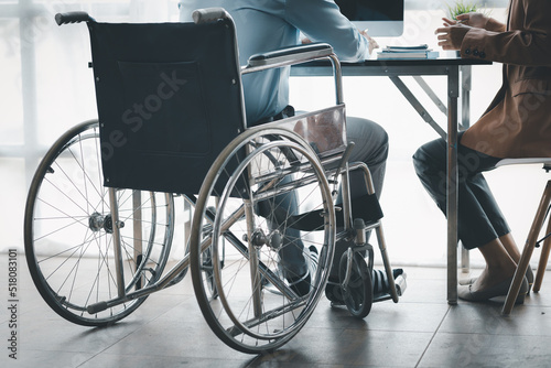 Man sits in wheelchair and brainstorms with colleagues, male and female employees working together in the office, working as a team in a large organization. The concept of team management is diverse.