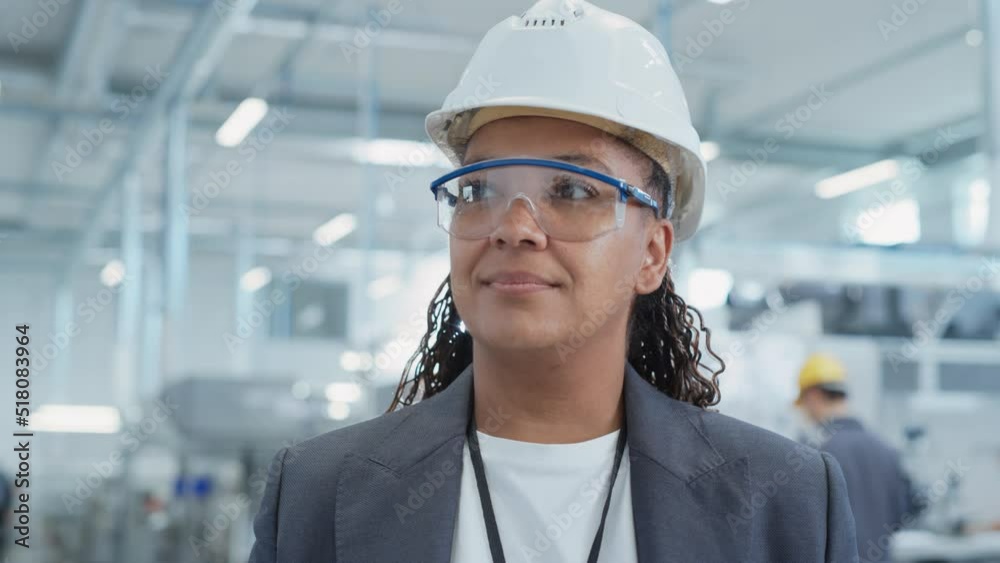 Close Up Portrait of a Happy and Smiling Middle Aged African Female Engineer in White Hard Hat Standing at Electronics Manufacturing Factory. Black Heavy Industry Specialist Posing for Camera. Close Up Portrait of a Happy and Smiling Middle Aged African Female Engineer in White Hard Hat Standing at Electronics Manufacturing Factory. Black Heavy Industry Specialist Posing for Camera.