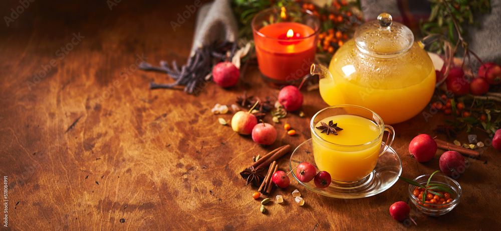 Glass teapot and cup with sea buckthorn tea with spices and autumn small crabapples on wooden background