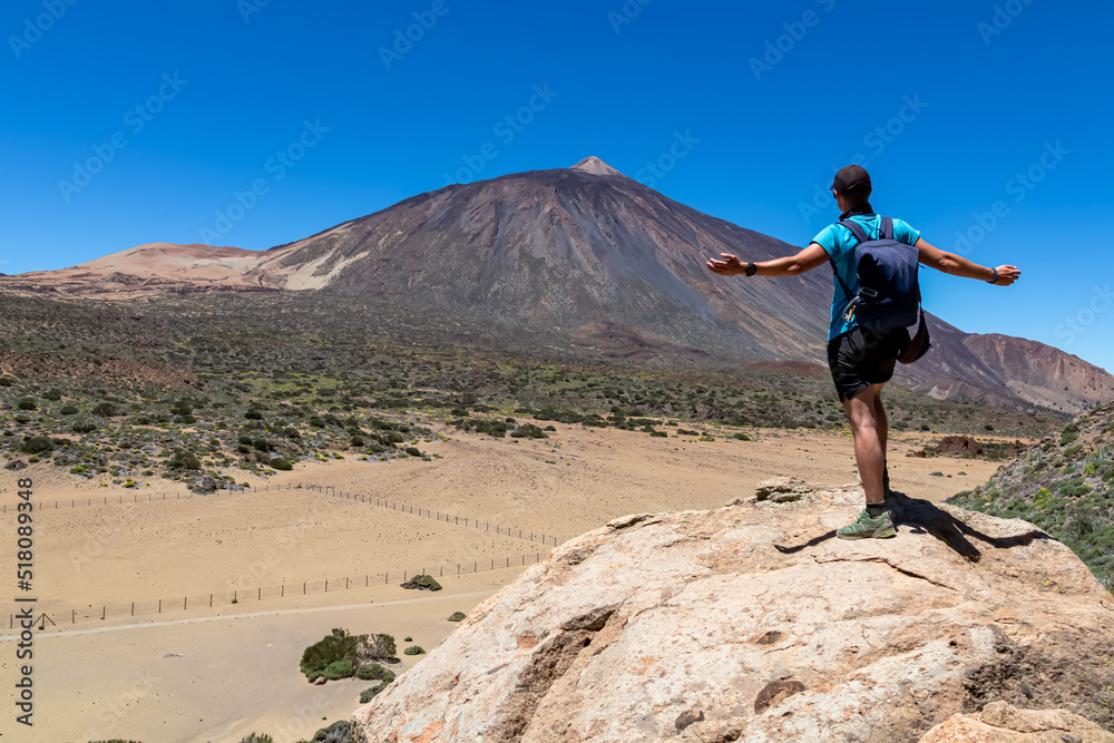 Man on rock with view on La Canada de los Guancheros dry desert plain and volcano Pico del Teide, Mount Teide National Park, Tenerife, Canary Islands, Spain, Europe. Hiking to Riscos de la Fortaleza