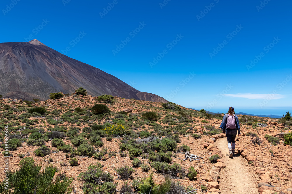 Woman on hiking trail to summit Riscos de la Fortaleza with scenic view on volcano Pico del Teide, Mount Teide National Park, Tenerife, Canary Islands, Spain, Europe. Via La Canada de los Guancheros