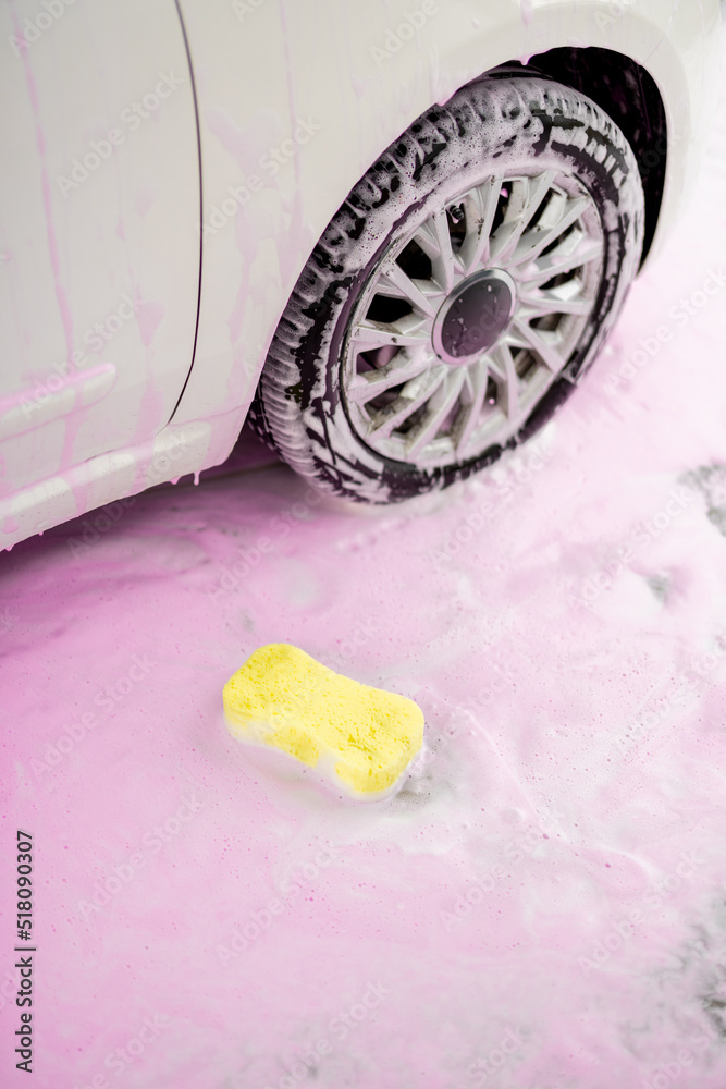 Yellow sponge in pink foam on the ground near vehicle wheel at car wash Yellow sponge in pink foam on the ground near vehicle wheel at car wash