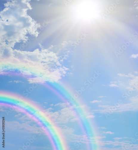 Miraculous beautiful double rainbow sunburst cloudscape background - big sun against blue sky and puffy clouds with a stunning double rainbow ideal for a special announcement or holistic spiritual bac
