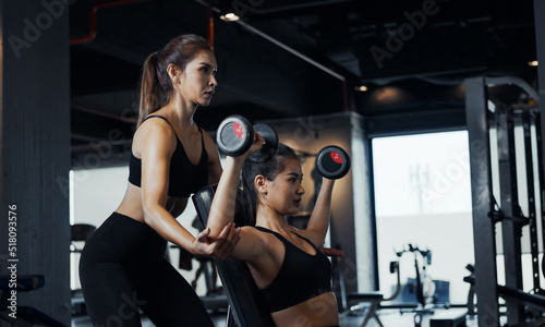 Fotografie Sporty girl doing weight exercises with the help of her personal trainer at the gym