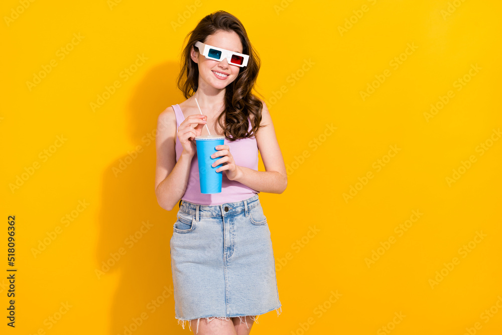 Portrait of attractive cheerful wavy haired girl watching film drinking soda isolated over bright yellow color background Portrait of attractive cheerful wavy haired girl watching film drinking soda isolated over bright yellow color background
