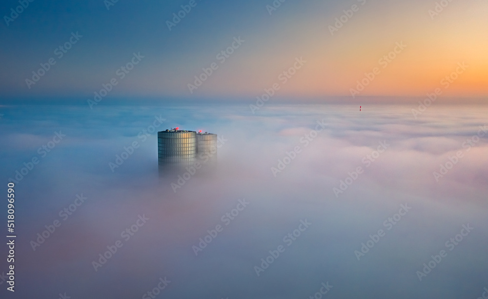 Skyscraper rooftop over the clouds at sunrise. Thick fog covers the Riga city, and warm sunlight over the clouds and church tower.
