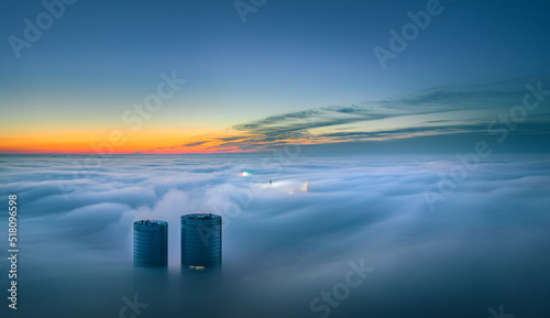 Skyscraper rooftop over the clouds at sunrise. Thick fog covers the Riga city, and warm sunlight over the clouds and church tower.