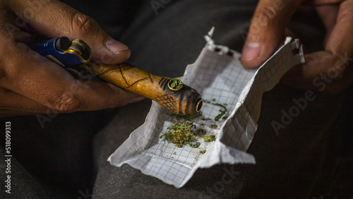 A wooden pipe for smoking marijuana and a lighter in the hands of a man in close-up on a blurry background. A man fills a smoking pipe with cannabis to smoke. Legalization of marijuana.Smoking pipe.
