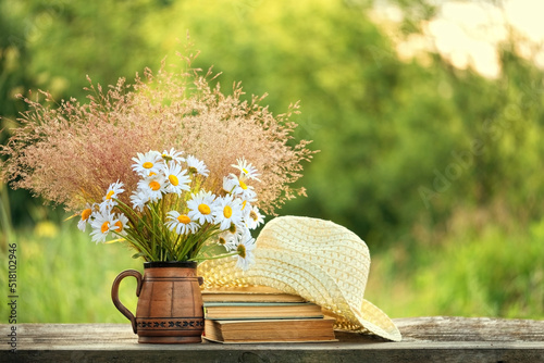 Chamomile flowers, book and summer hat on table in sunny garden. Harmony, peaceful mood, relax time. summer season concept. Rustic composition photo