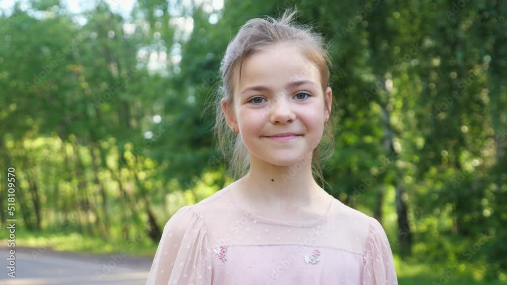 Teen girl looks straight on big forest pathway. Schoolgirl wearing pink dress shows thumb-up smiling closeup. Girl enjoys walking Teen girl looks straight on big forest pathway. Schoolgirl wearing pink dress shows thumb-up smiling closeup. Girl enjoys walking