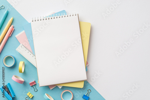 Back to school concept. Top view photo of stack of notebooks pens ruler stapler binder clips and adhesive tape on bicolor blue and white background with blank space