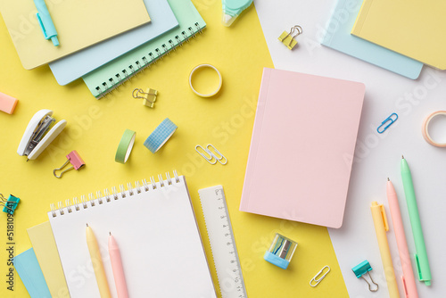 School accessories concept. Top view photo of colorful notebooks sharpener ruler corrector pens binder clips adhesive tape and stapler on bicolor yellow and white background