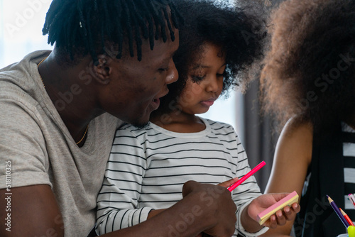 A black american father  his daughters are doing their homework in the living room.
