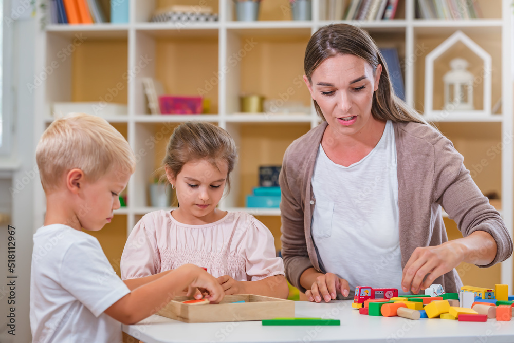 Kindergarten teacher playing together with children in the colorful preschool classroom. Mother playing with children. Kindergarten teacher playing together with children in the colorful preschool classroom. Mother playing with children.
