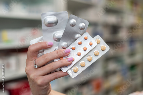 Pharmacist's hand holding many different pills near the chest of shelves with medicines.