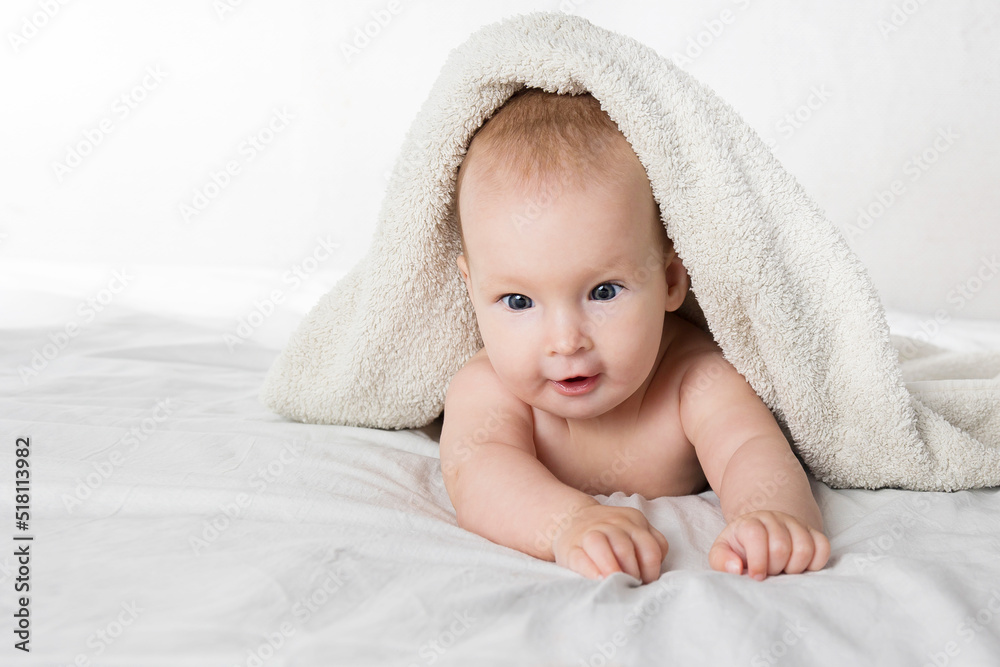 A half-year-old cute baby in a diaper and a towel lies on his stomach and looks cheerfully at the camera A half-year-old cute baby in a diaper and a towel lies on his stomach and looks cheerfully at the camera