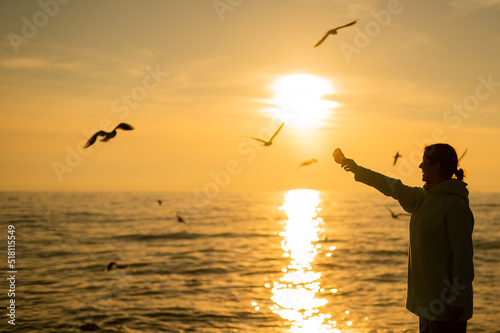 Caucasian woman feeding seagulls on the sea at sunset. 