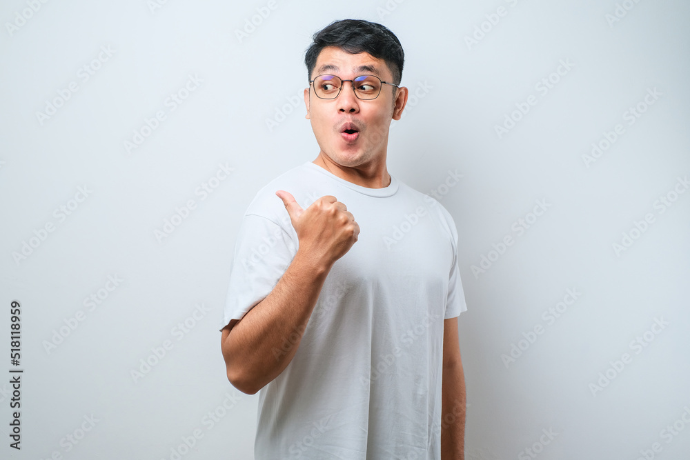 Young asian man surprised pointing with hand finger to the side, open mouth amazed expression. Young asian man surprised pointing with hand finger to the side, open mouth amazed expression.
