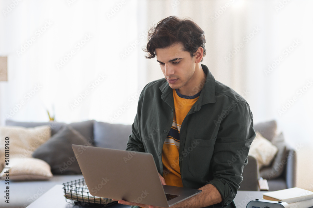Confident freelance programmer standing in the office or coworking working using laptop. Concentrated male young entrepreneur with computer, looking at the screen. Distant work Confident freelance programmer standing in the office or coworking working using laptop. Concentrated male young entrepreneur with computer, looking at the screen. Distant work