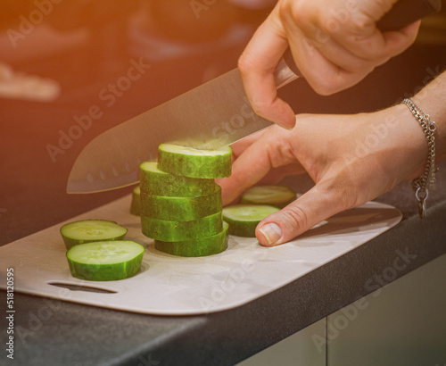 The cook in the kitchen at work prepares a vegetable salad and cuts a green cucumber. The girl is engaged in slicing cucumbers on a cutting board. A woman cuts vegetables for a salad. 