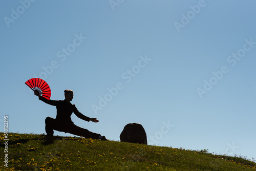 Asian woman with fan practicing taijiquan at sunset, chinese martial arts, healthy lifestyle concept.