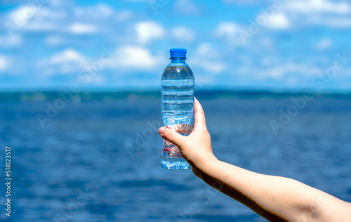 A girl holds a bottle of drinking water in her hand against a blue sky background