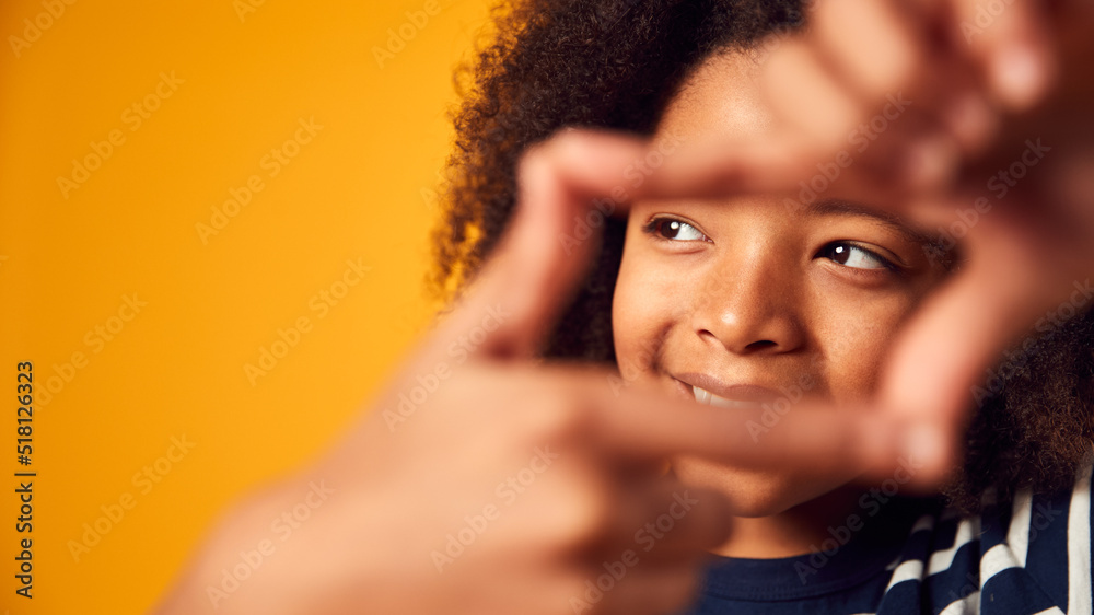 Fototapeta premium Studio Portrait Of Smiling Boy Making Shape Of Picture Frame With Hands Against Yellow Background