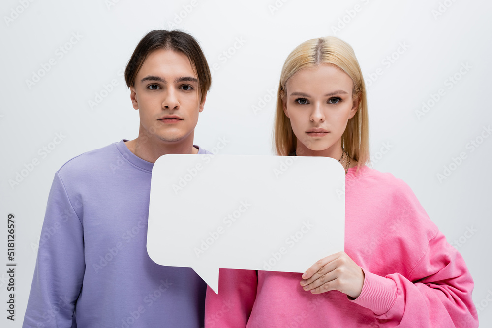 Young couple in sweatshirts holding white speech bubble isolated on grey. Young couple in sweatshirts holding white speech bubble isolated on grey.