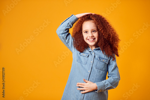 Studio Shot Of Girl Patting Head And Rubbing Stomach Against Yellow Background photo