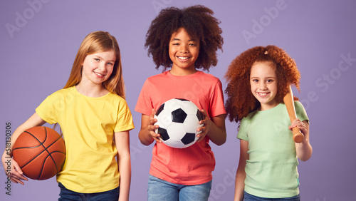 Studio Shot Of Children With Sports Equipment For Soccer Basketball Baseball On Purple Background