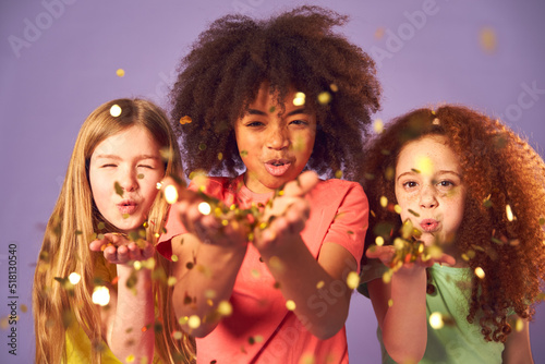 Studio Shot Of Children Blowing Glitter From Hands On Purple Background