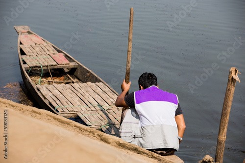Young man getting ready to sail the wooden boat to the river. Young boy holding the paddle of the boat to float on the lake by wooden boat. Man sitting on the boat.