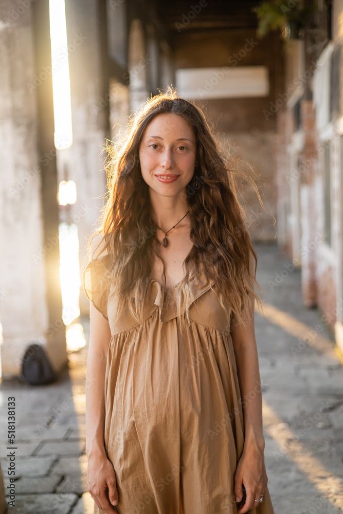 Portrait of smiling pregnant woman in sunlight looking at camera outdoors in Venice.