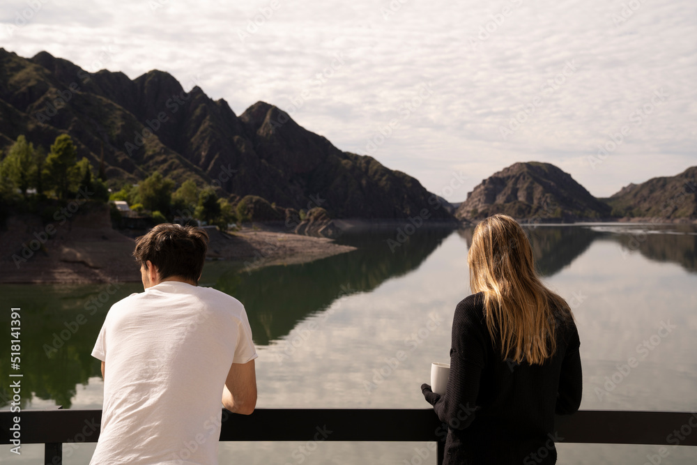 Tourism. Young couple on vacations. View of a young man and woman, contemplating the beautiful view of the lake and mountains, in a sunny day. 