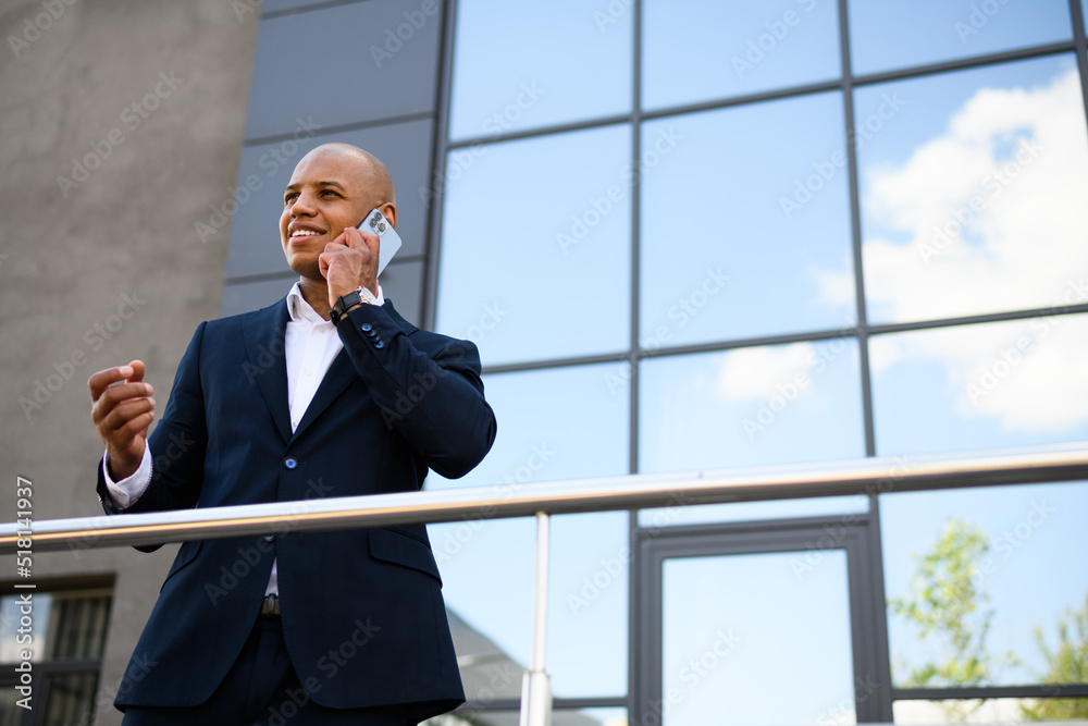 Positive african american businessman in suit talking on smartphone on urban street Positive african american businessman in suit talking on smartphone on urban street