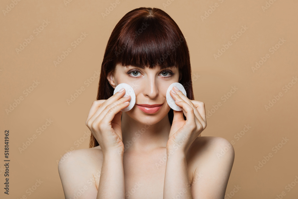 Portrait of beautiful positive young woman with red hair and bare shoulders posing in studio with cotton pads in hands. Concept of people, cosmetic and skin care. Portrait of beautiful positive young woman with red hair and bare shoulders posing in studio with cotton pads in hands. Concept of people, cosmetic and skin care.