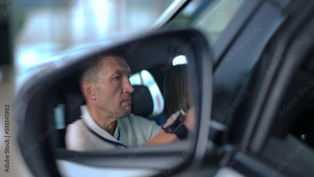 Close-up side view mirror with reflection of Caucasian man and woman sitting in car choosing vehicle in dealership. Successful confident couple examining automobile salon thinking. Choice and success Close-up side view mirror with reflection of Caucasian man and woman sitting in car choosing vehicle in dealership. Successful confident couple examining automobile salon thinking. Choice and success