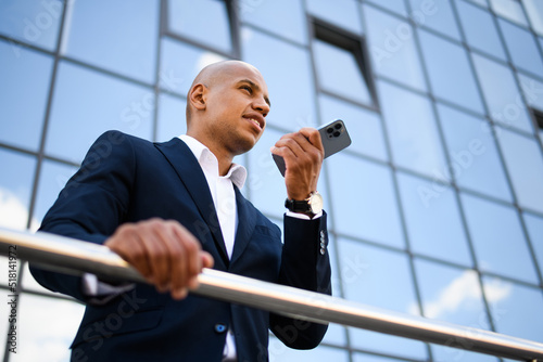 Low angle view of african american businessman recording voice message on smartphone on street 