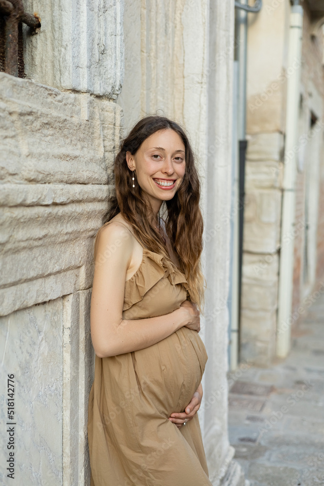 Cheerful pregnant woman looking at camera ear old building in Italy.
