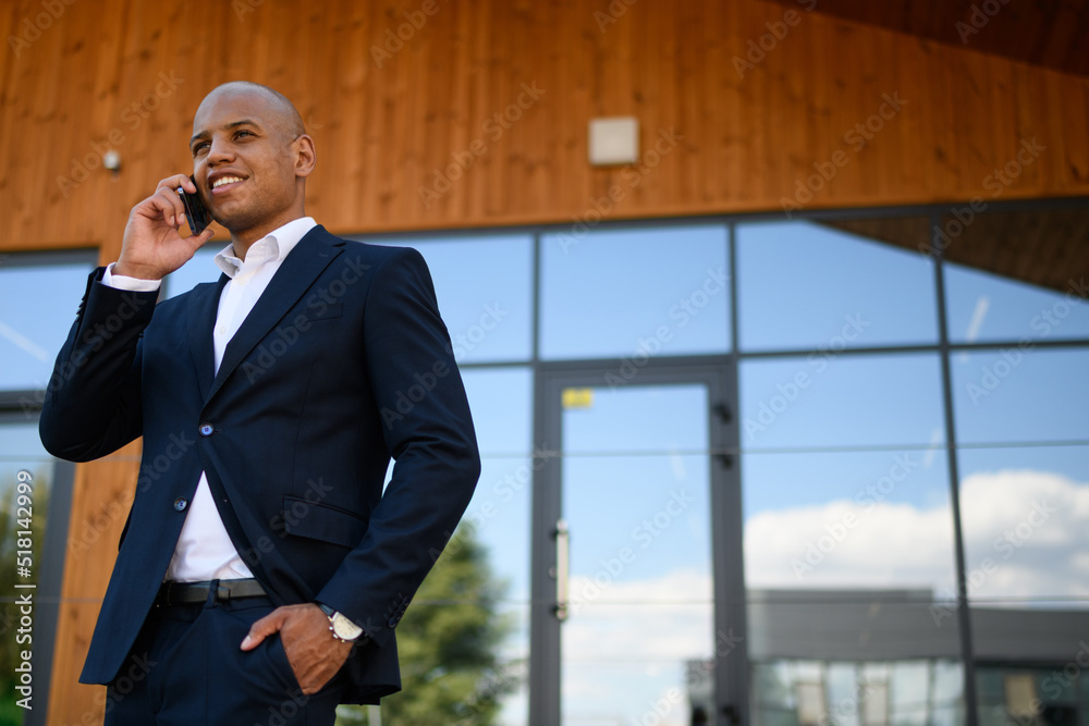 Low angle view of african american realtor talking on smartphone near building Low angle view of african american realtor talking on smartphone near building